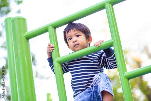 Asian preschool boy climbing on playground climb bar in city public park morning activity