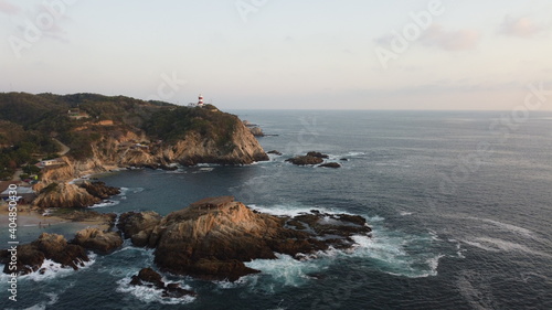 Vista aérea de las olas del mar rompiendo en las rocas y un faro sobre el acantilado 