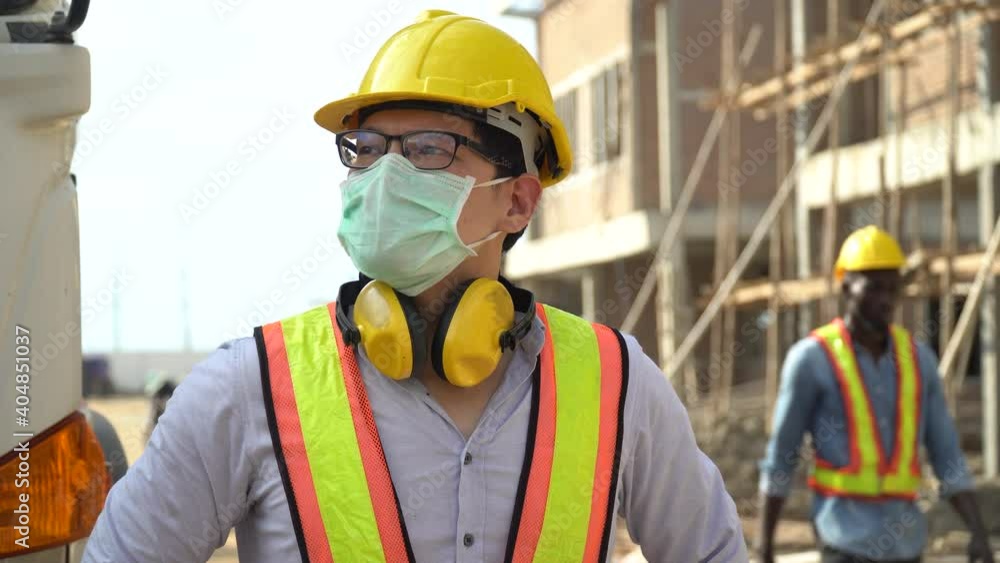 asian builder in hard hat wearing protective face mask in construction site. asian builder in hard hat wearing protective face mask in construction site.