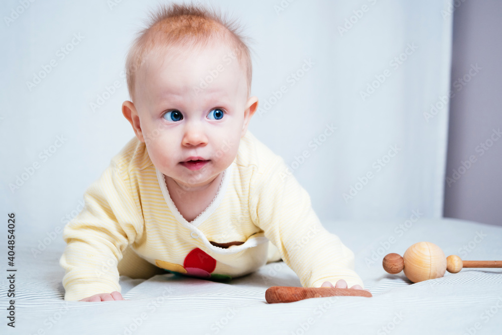 Portrait of a cute seven-month-old girl with blue eyes. A child plays with wooden toys in a bright room. Eco-friendly toys for children made from natural materials Portrait of a cute seven-month-old girl with blue eyes. A child plays with wooden toys in a bright room. Eco-friendly toys for children made from natural materials