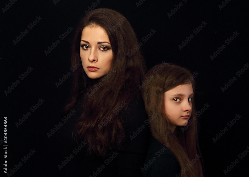 Beautiful concentrated serious mother and her angry emotional thinking daughter looking on black shadow background. Concept family