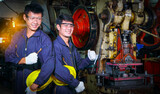 Two skilled Asian workers, dressed in helmet uniforms, are discussing machine repair analysis.