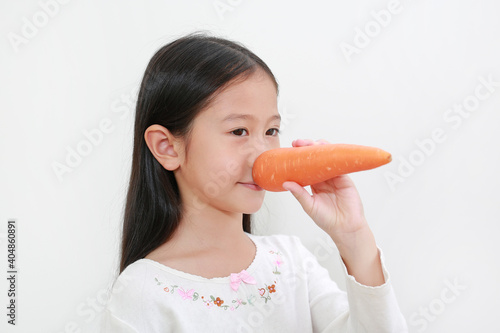 Cute little asian child girl making long nose with carrot isolated on white background