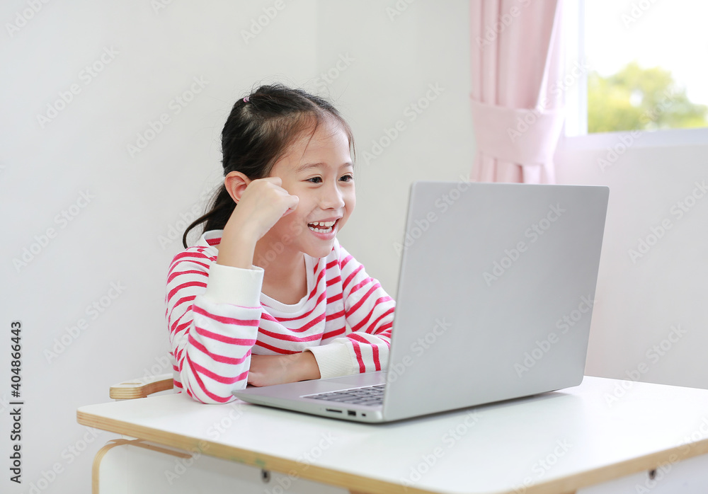 Asian little child girl sitting at desk enjoy watching cartoon on laptop computer stay at home Asian little child girl sitting at desk enjoy watching cartoon on laptop computer stay at home