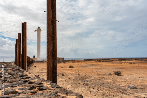 Lighthouse in the distance seen behind a low stone construction with exposed metal beams photo