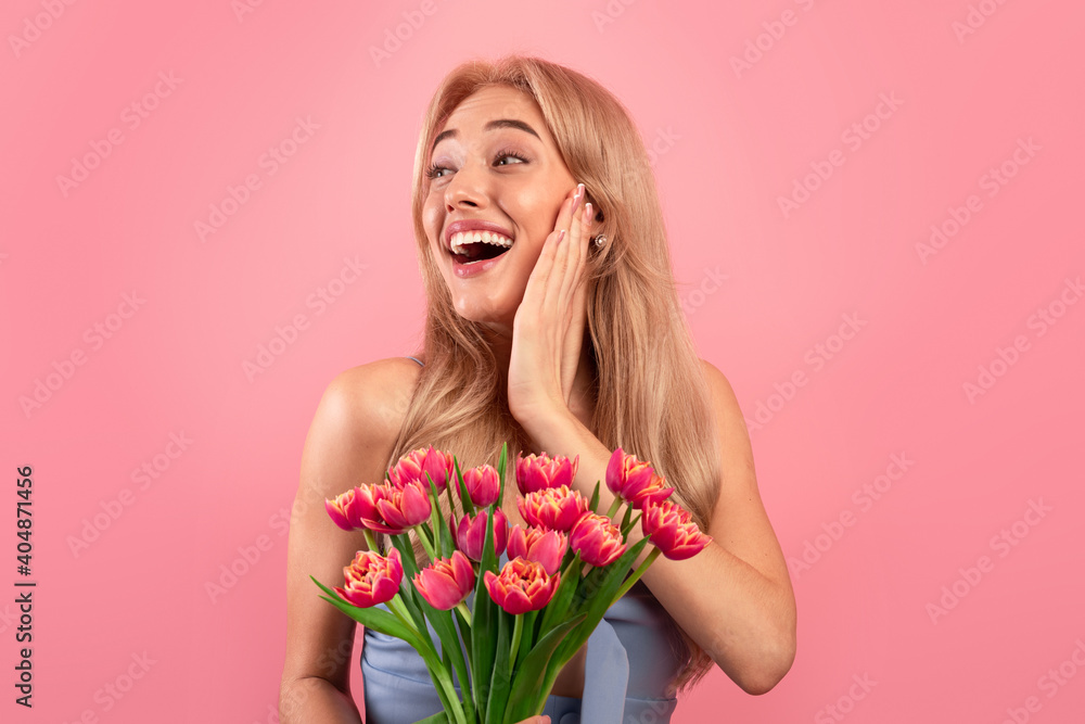 Portrait of beautiful young lady with lovely flowers feeling excited on pink studio background. Spring holiday concept