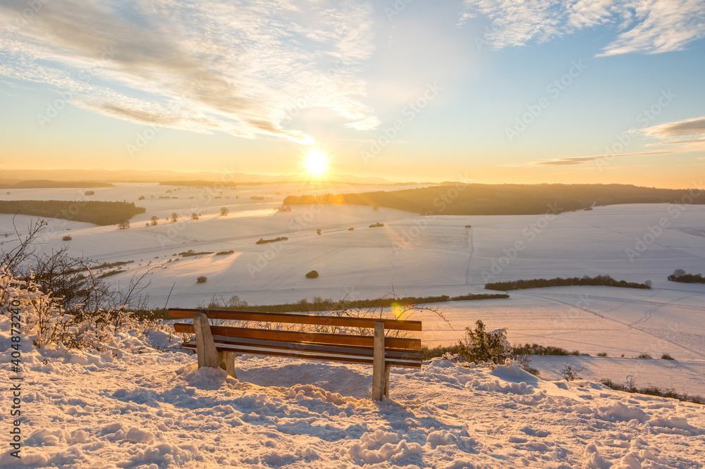 Scenic colourful sunset over beautiful winter landscape in the Swabian Alps with bench in the foreground