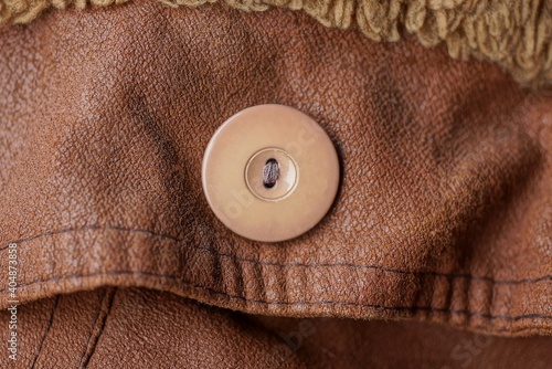 one large plastic round button on a leather brown jacket