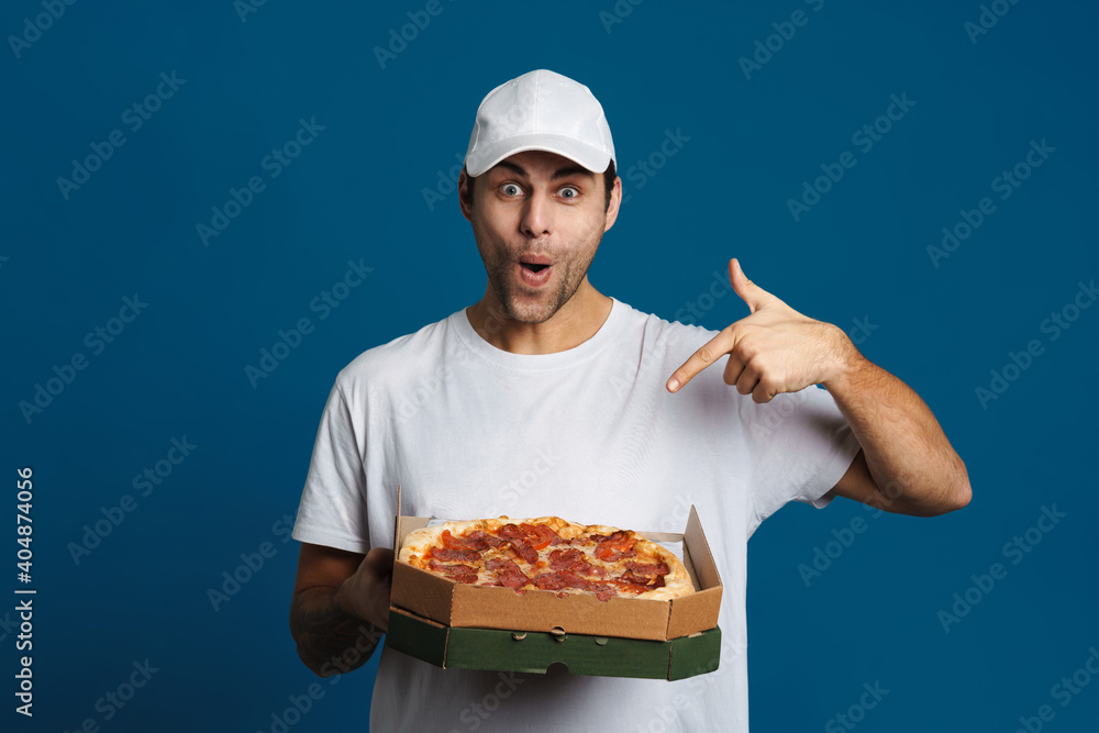 Delighted caucasian delivery man holding and pointing finger at pizza Delighted caucasian delivery man holding and pointing finger at pizza