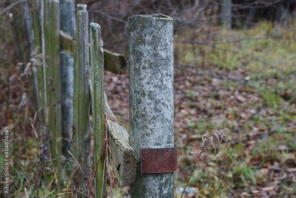 part of a destroyed old fence made of wooden boards and a gray concrete pillar on a rural street part of a destroyed old fence made of wooden boards and a gray concrete pillar on a rural street