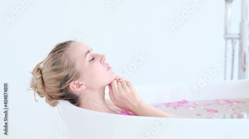 Beautiful Caucasian Blonde Girl In Bikini Lying In Flower Bath In Resort Day Spa Salon. Skin Care Therapy. Concept young woman relaxing in the bathtube.
