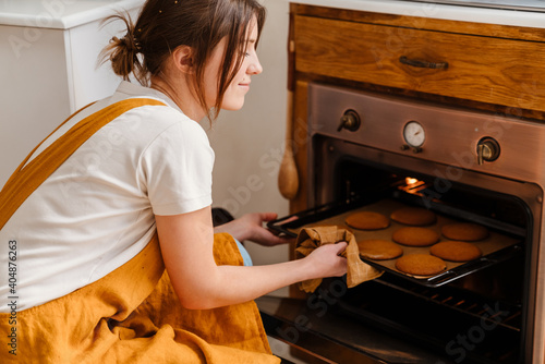 Foto Caucasian pleased pastry chef woman baking cookies at cozy kitchen
