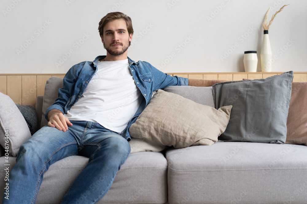 Handsome young man looking thoughtful while sitting on the couch at home