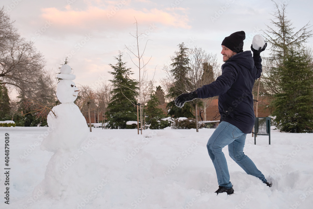 Young caucasian man destroying a smiley snowman with a hat during Filomena snowstorm in Madrid, Spain. Winter activities.