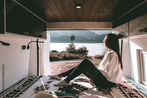 Image of a young brunette woman, resting inside a camper, in the mountains and a river
