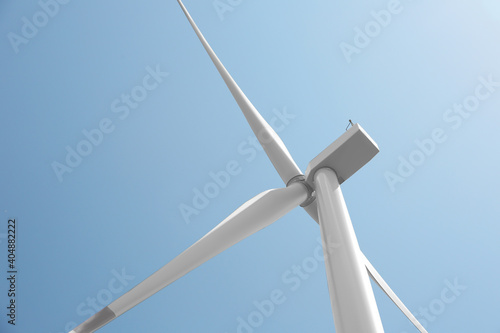 Modern wind turbine against blue sky, low angle view. Energy efficiency