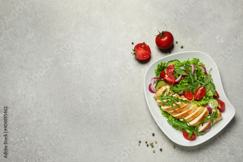 Delicious salad with meat, arugula and vegetables on grey table, flat lay. Space for text