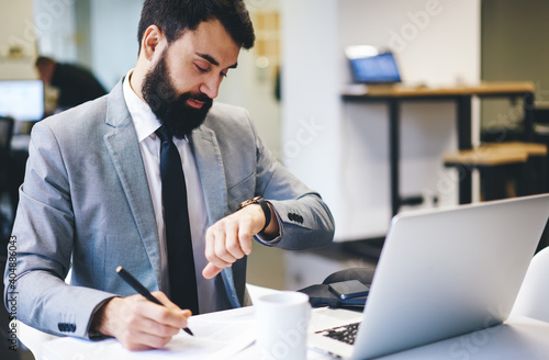 Pensive businessman looking at wristwatch while working in office