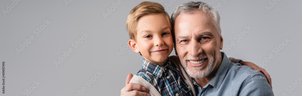 happy granddad and grandson hugging while smiling at camera isolated on grey, banner happy granddad and grandson hugging while smiling at camera isolated on grey, banner