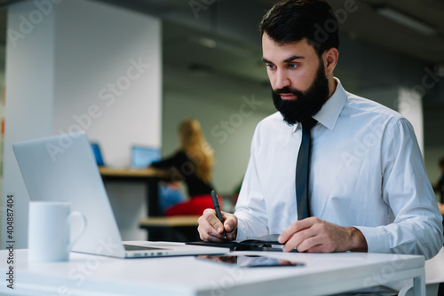 Focused businessman taking notes from laptop while working in modern workspace
