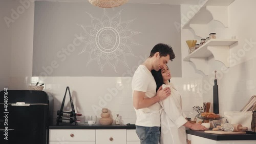young man seducing and embracing girlfriend drinking coffee in kitchen