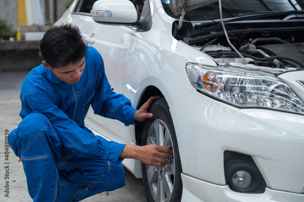 Asian car mechanic technician sitting and checking car tyres or car wheel in in auto repair shop garage. Wheel tire repair service. Asian car mechanic technician sitting and checking car tyres or car wheel in in auto repair shop garage. Wheel tire repair service.