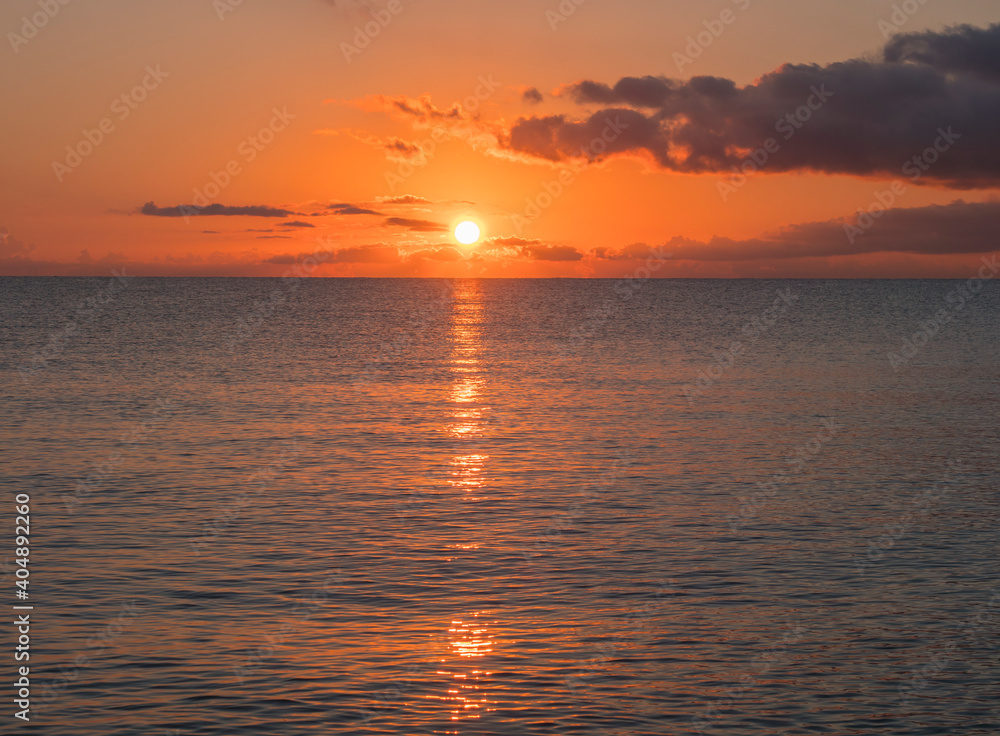 Sunrise with the red orange sun raising up from the sea with dark clouds at beach Spiaggia di Santa Maria Navarrese, Sardinia, Italy