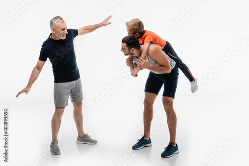 cheerful grandfather imitating plane near dad piggybacking kid on white