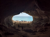 View from inside of limestone sea cave at Cala Luna beach, Sardinia, Italy with group of tourist people sunbathing and takes photos. Famous touristic destination