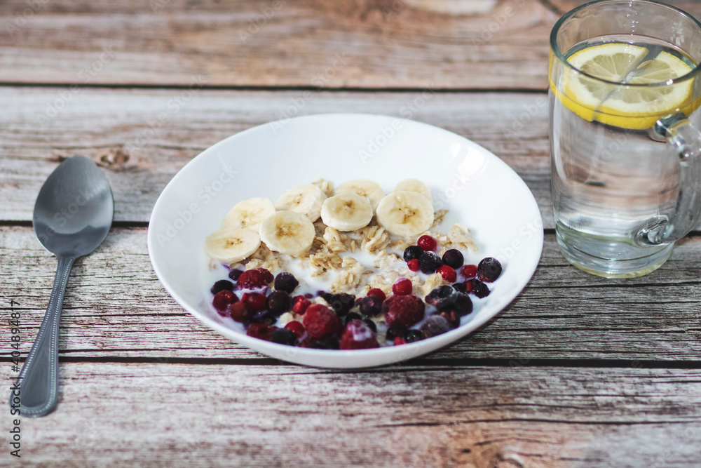 Oatmeal with banana pieces and berries, drenched in milk. Next to a glass of water with lemon Oatmeal with banana pieces and berries, drenched in milk. Next to a glass of water with lemon