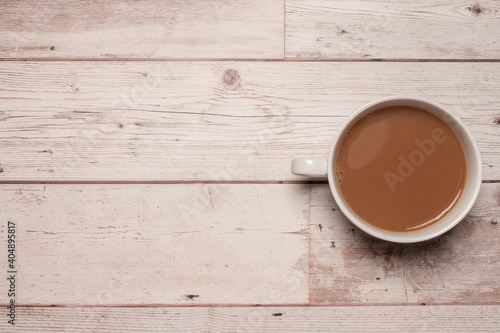 Cup of strong tea or coffee with milk in a white mug on a textured white wooden table surface with copy space and room for text