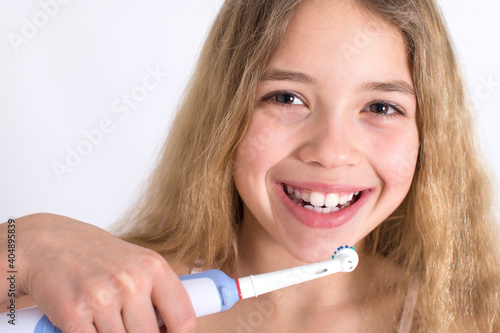 Young girl portrait with rotating-oscillating electric toothbrush isolated on white background. Oral hygiene and white teeth concept.