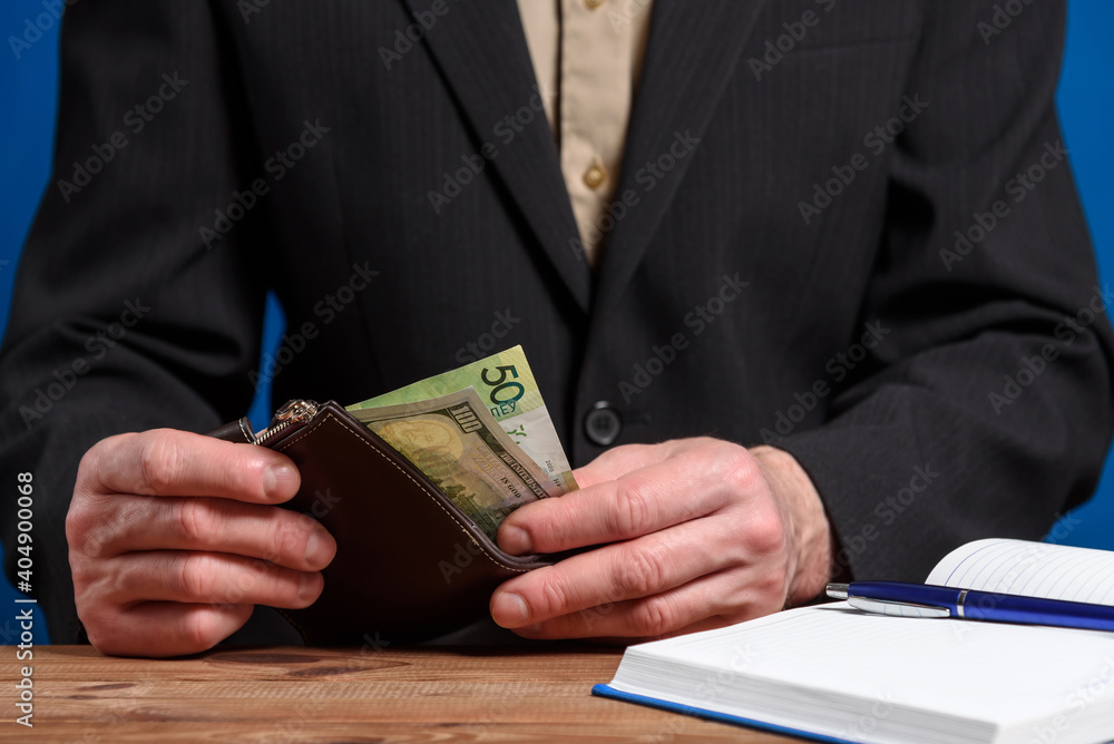 A man in a suit holds a wallet. Men's hands take out or put a bill in a wallet.
A man in a suit holds a wallet. Men's hands take out or put a bill in a wallet.