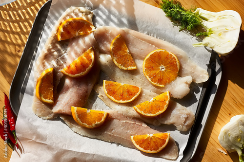 Cod fish fillet with oranges on baking paper. Seafood, healthy eating. Natural light. Top view.