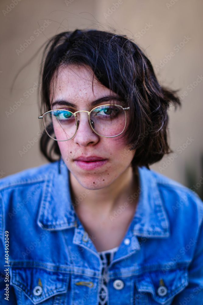 Portrait of young woman with blond hair in the city, using glasses, with denim jacket Portrait of young woman with blond hair in the city, using glasses, with denim jacket