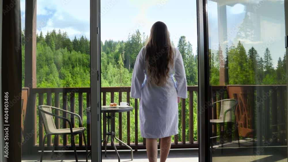 Young woman in bathrobe walking out of hotel room on terrace and stretching out hands. Concept of tourism and vacation in mountains at summer Young woman in bathrobe walking out of hotel room on terrace and stretching out hands. Concept of tourism and vacation in mountains at summer