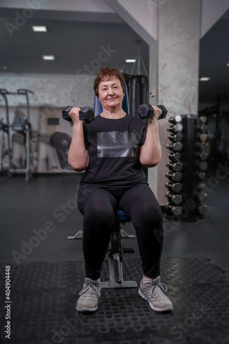 an elderly woman in the gym is engaged in fitness with dumbbells in her hands