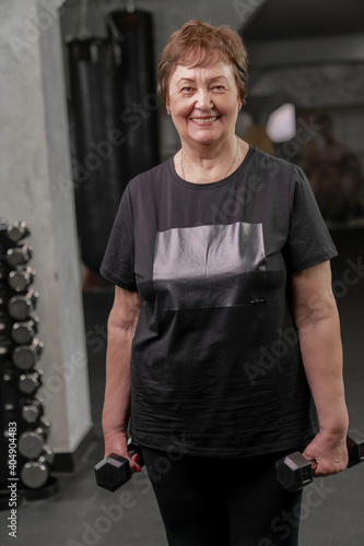 an elderly woman in training with a smile holds dumbbells in her hands