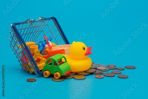 Coins and shopping basket full of toys. Cost of buying toys and parenting expenses concept