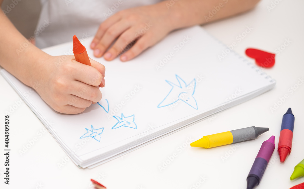 A little girl in a white T-shirt draws with wax crayons at the table at home. A little girl in a white T-shirt draws with wax crayons at the table at home.