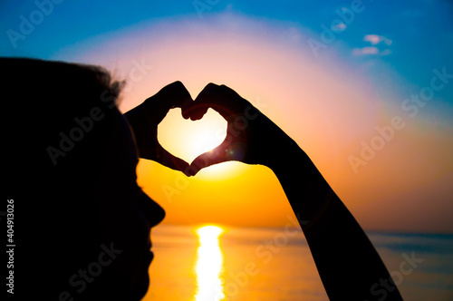 Silhouette hand in heart shape with sunrise in the middle and sea background