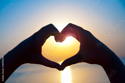 Silhouette hand in heart shape with sunrise in the middle and sea background