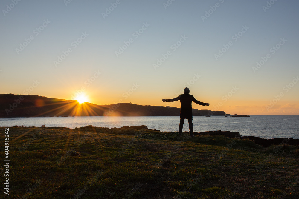 Man looking out to sea at sunset with open arms