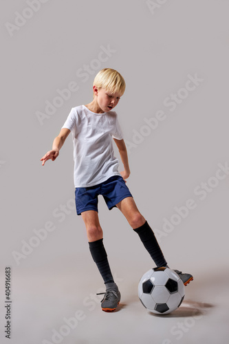 boy soccer player playing with ball, kicking it, training before match. isolated in studio, wearing uniform © Roman