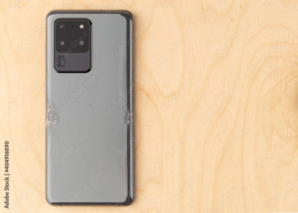 Smartphone with a broken back cover on a wooden background. Smartphone with a broken back cover on a wooden background.
