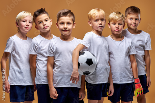 football team of successful members in sportive uniform looking at camera. caucasian kids enjoy sportive games, posing with soccer ball in hands © Roman