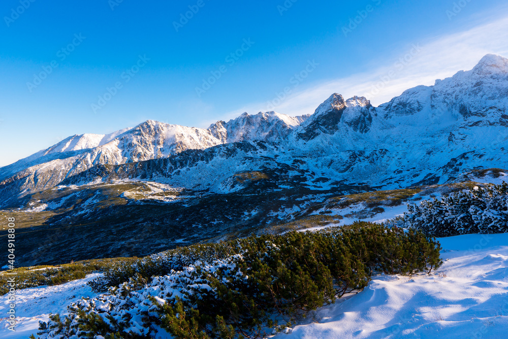 Winter mountain landscape. Sun shines through mountain peak at snowy hills. Winter scene in Tatra mountains, Poland.