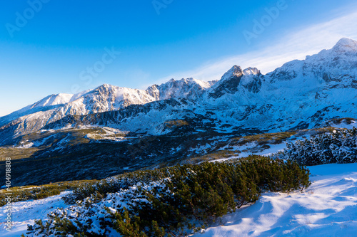 Winter mountain landscape. Sun shines through mountain peak at snowy hills. Winter scene in Tatra mountains, Poland.