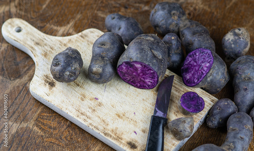 Obraz na płótnie Vitelotte, french purple potatoes sliced in half with a knife on wooden board at rustic kitchen table. Blue variety of popular potato w salonie