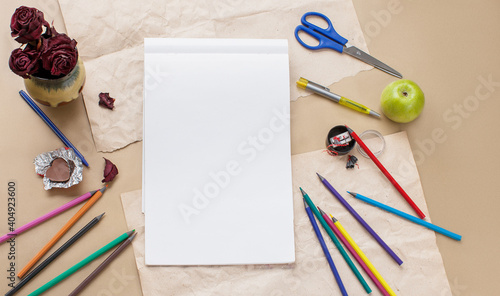 Album sheet  blank paper on desk  flat lay with colored pencils, flowers, sweet, scissors and a sharpener
